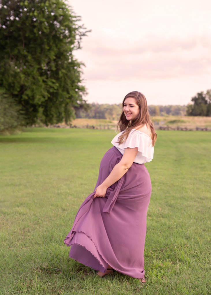 Pregnant woman twirling in a field in Yorktown, Virginia getting her maternity portraits taken by a Yorktown maternity photographer.